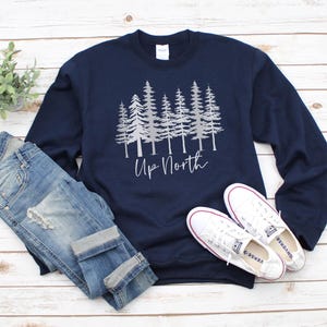 May include: A navy blue long-sleeved sweatshirt with a silver graphic of a row of pine trees and the text "Up North".