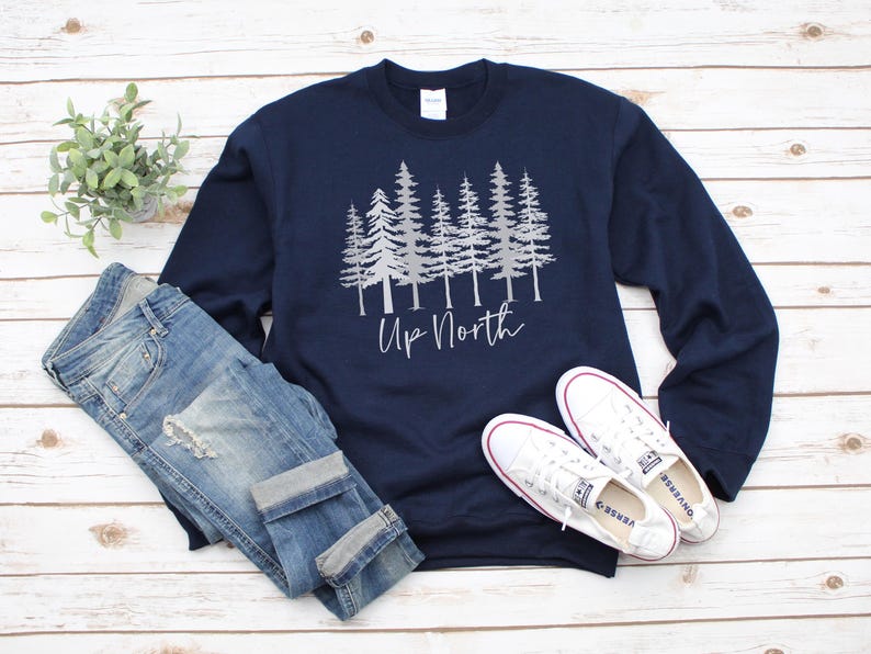 May include: A navy blue long-sleeved sweatshirt with a silver graphic of a row of pine trees and the text "Up North".