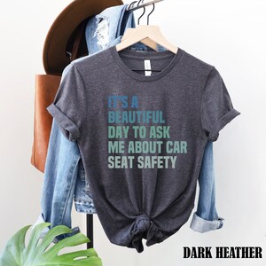 K&ouml;nnte beinhalten: Dunkelgraues T-Shirt mit dem Text "It's a beautiful day to ask me about car seat safety" in einem Farbverlauf von Blau, Gr&uuml;n und T&uuml;rkis.