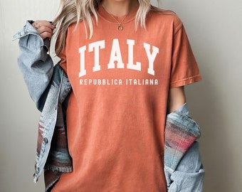 May include: A burnt orange t-shirt with the word "ITALY" in white block letters and the text "REPUBBLICA ITALIANA" in smaller white letters below.