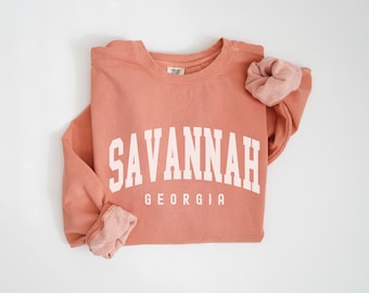 Könnte beinhalten: Ein pfirsichfarbener Pullover mit dem Text "SAVANNAH GEORGIA" in Weiß.