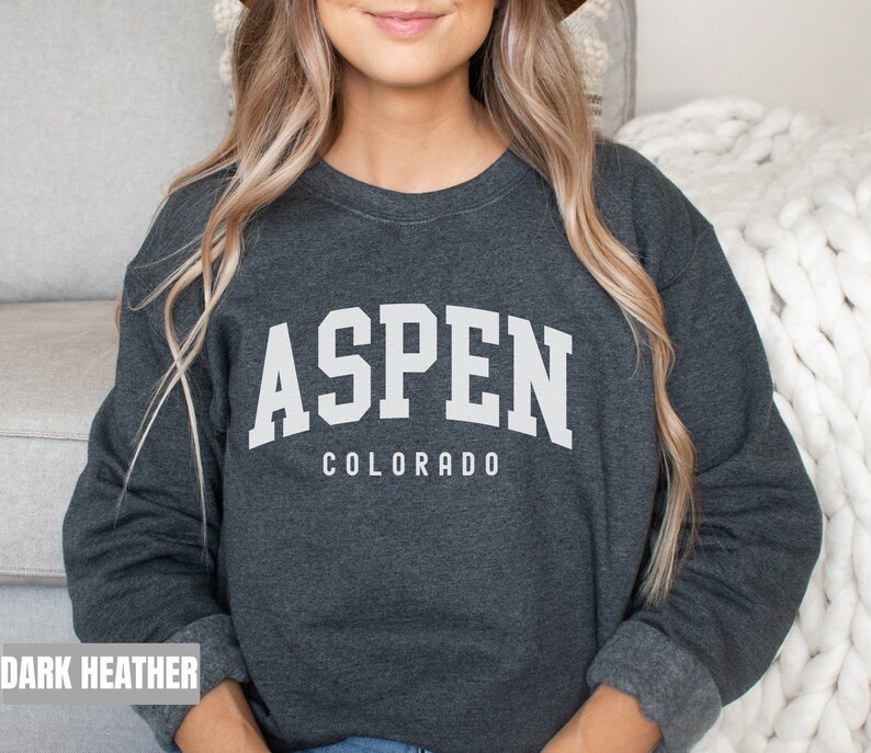 May include: Dark heather grey sweatshirt with white text that reads "Aspen Colorado" in a collegiate font.