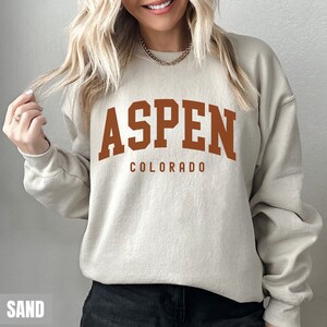 May include: A beige sweatshirt with the text "ASPEN COLORADO" printed in brown on the front.