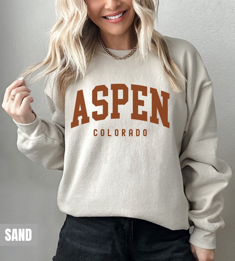 May include: A beige sweatshirt with the text "ASPEN COLORADO" printed in brown on the front.