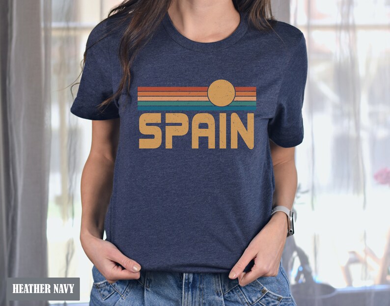 May include: A heather navy blue t-shirt with a vintage-style graphic of a sunset over a striped horizon with the word "SPAIN" in a retro font.