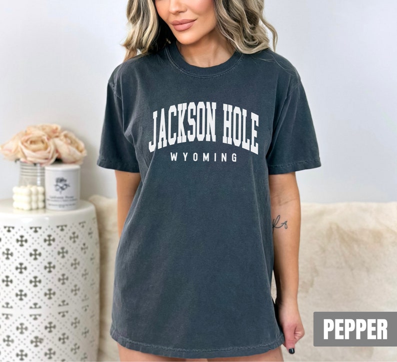 May include: A dark gray t-shirt with the text "JACKSON HOLE WYOMING" in white. The shirt is a relaxed fit and has a crew neck.