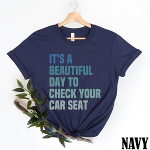 May include: Navy blue t-shirt with the text "It's a beautiful day to check your car seat" in a gradient of blue and green.