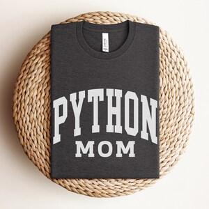 Peut inclure: Un t-shirt gris fonc&eacute; avec le texte "PYTHON MOM" en lettres blanches.