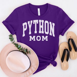 Peut inclure: T-shirt violet avec un texte blanc qui dit "PYTHON MOM" dans une police d'&eacute;criture universitaire.