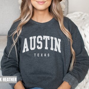 May include: Dark heather grey sweatshirt with the text "AUSTIN TEXAS" in white.