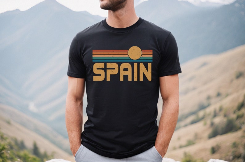 May include: A black t-shirt with a vintage-style graphic design featuring a sunset with a yellow sun and the word "SPAIN" in a retro font.