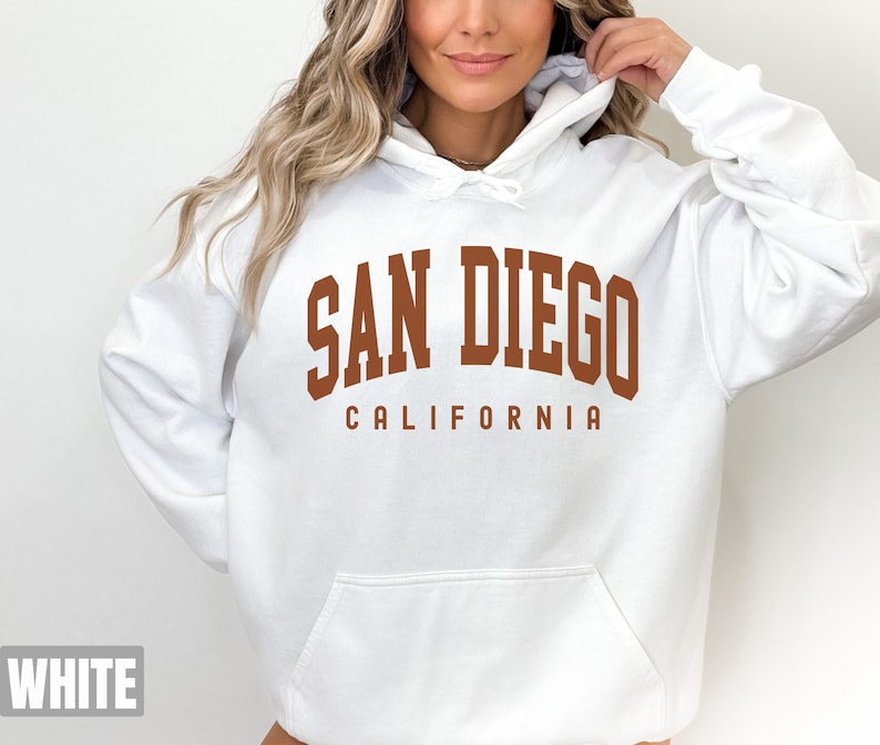 Pode incluir: Moletom branco com capuz com uma estampa marrom que diz "San Diego California".
