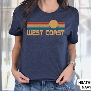 May include: A heather navy blue t-shirt with a retro sunset graphic and the text "WEST COAST" in a yellow font.