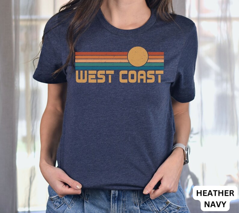 May include: A heather navy blue t-shirt with a retro sunset graphic and the text "WEST COAST" in a yellow font.