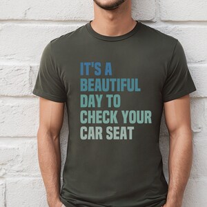 May include: A dark green t-shirt with the text "It's a beautiful day to check your car seat" in a gradient of blue and green.