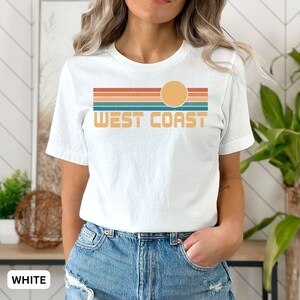 May include: White t-shirt with a retro sunset graphic and the text "West Coast" in orange.