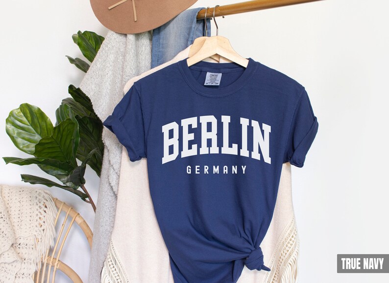 Pode incluir: Uma camiseta azul marinho com texto branco que diz "BERLIM ALEMANHA".