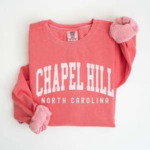 May include: A coral pink sweatshirt with the text "Chapel Hill North Carolina" in white.
