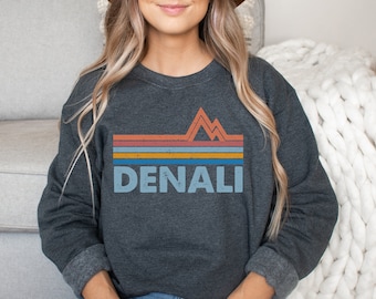 May include: A dark gray sweatshirt with a vintage-style graphic of mountains and the word "DENALI" in a faded blue color.