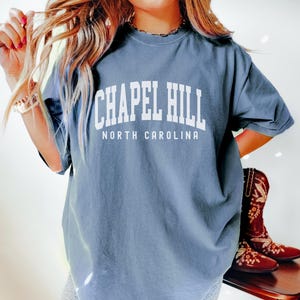 Op de afbeelding: Een oversized blauw t-shirt met witte tekst die "Chapel Hill North Carolina" zegt.