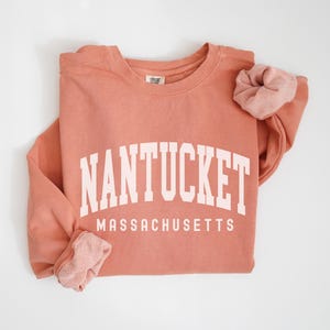 May include: A coral colored sweatshirt with the text "NANTUCKET MASSACHUSETTS" in white.