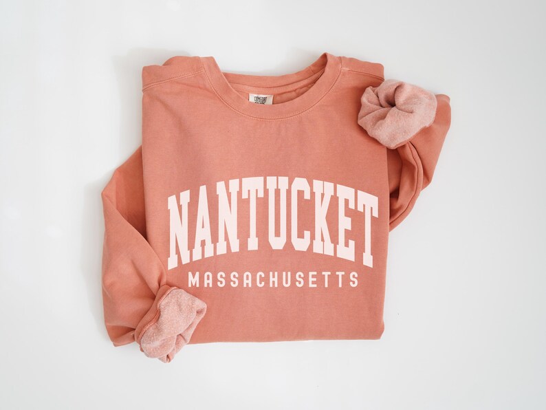 May include: A coral colored sweatshirt with the text "NANTUCKET MASSACHUSETTS" in white.