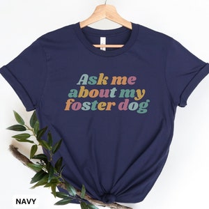 May include: A navy blue t-shirt with the text "Ask me about my foster dog" in rainbow colors.