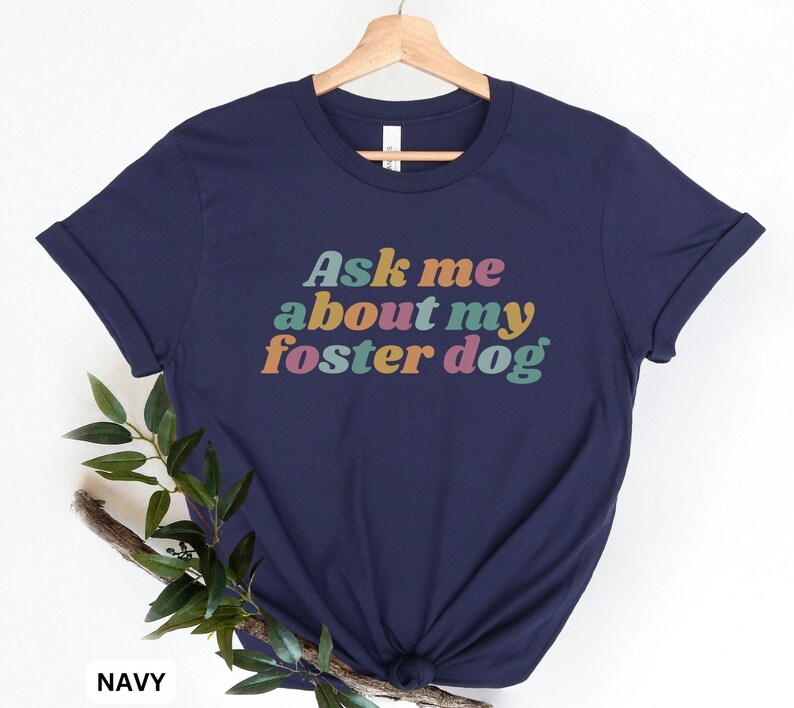 May include: A navy blue t-shirt with the text "Ask me about my foster dog" in rainbow colors.