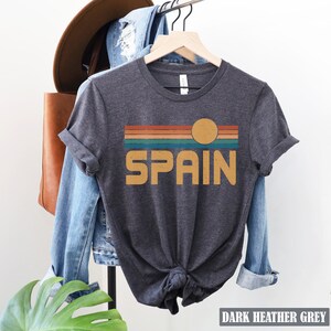 May include: Dark heather grey t-shirt with a retro sunset graphic and the word "SPAIN" in yellow.