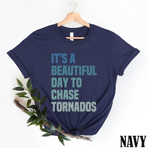 Könnte beinhalten: Marineblaues T-Shirt mit dem Text "It's a beautiful day to chase tornados" in einem Farbverlauf von Blau und Grün.