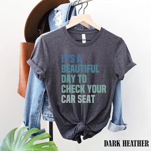 May include: Dark heather grey t-shirt with the text "It's a beautiful day to check your car seat" in a gradient of blue and green.