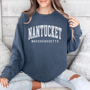 May include: A navy blue long-sleeved sweatshirt with the text "NANTUCKET MASSACHUSETTS" printed in white.