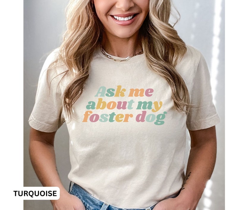 May include: A light beige t-shirt with the text "Ask me about my foster dog" in colorful, retro-style lettering.