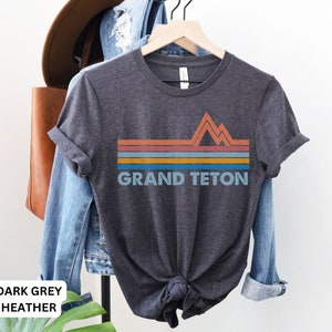 Puede incluir: Camiseta de color gris oscuro jaspeado con un gr&aacute;fico retro de monta&ntilde;as y el texto "GRAND TETON" en blanco.