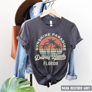 May include: Dark heather grey t-shirt with a vintage-style graphic of palm trees and a sunset. The graphic says "Sunshine Paradise Delray Beach Florida".
