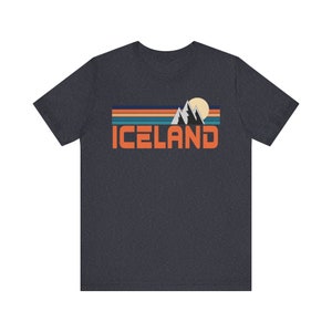 Puede incluir: Una camiseta gris oscuro jaspeada con un gr&aacute;fico retro de monta&ntilde;as, un sol y la palabra "ICELAND" en naranja.