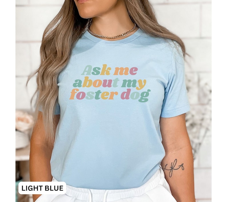 May include: Light blue t-shirt with the text "Ask me about my foster dog" in colorful retro-style lettering.