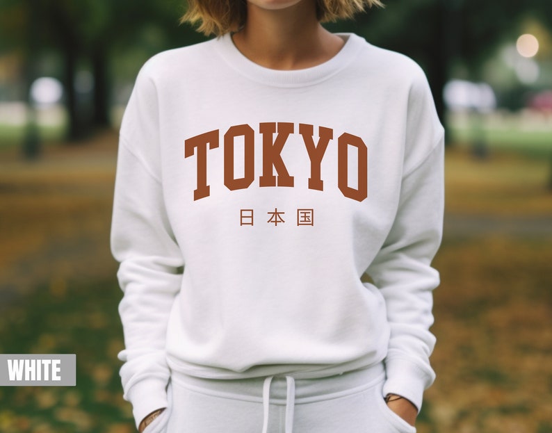 May include: White sweatshirt with a brown graphic print of the word "TOKYO" in a collegiate font with the Japanese characters for "Japan" underneath.