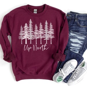 May include: A maroon sweatshirt with a white silhouette of a row of pine trees and the text "Up North" in pink lettering.
