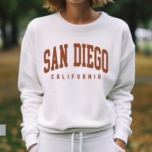Pode incluir: Camisola branca com o texto "SAN DIEGO CALIFORNIA" em letras castanhas.