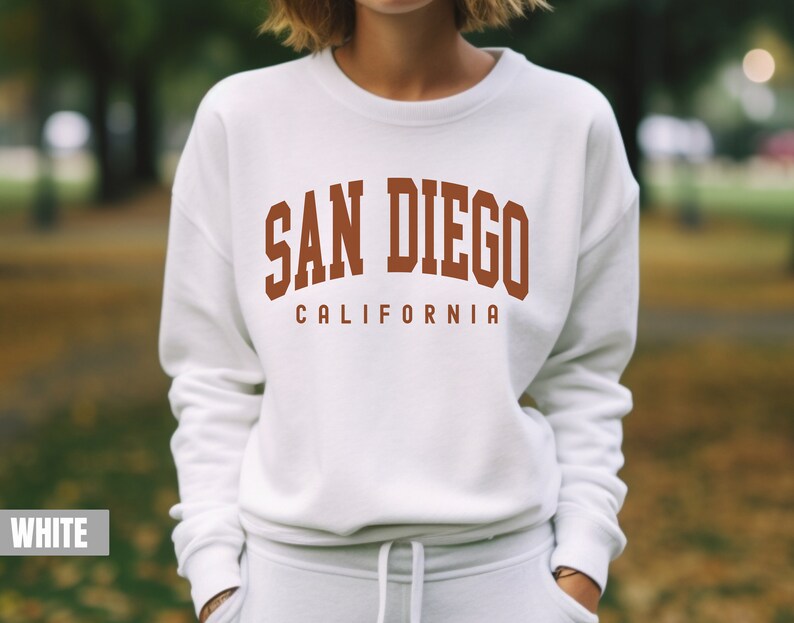 Pode incluir: Camisola branca com o texto "SAN DIEGO CALIFORNIA" em letras castanhas.