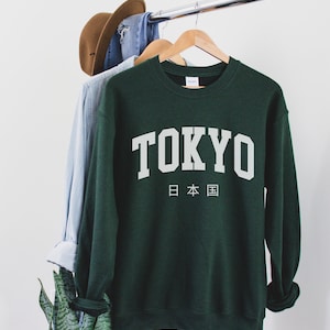 May include: A dark green sweatshirt with the word "TOKYO" printed in white on the front. Below the word "TOKYO" is the Japanese text for "Japan" in white.