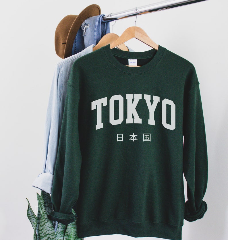 May include: A dark green sweatshirt with the word "TOKYO" printed in white on the front. Below the word "TOKYO" is the Japanese text for "Japan" in white.