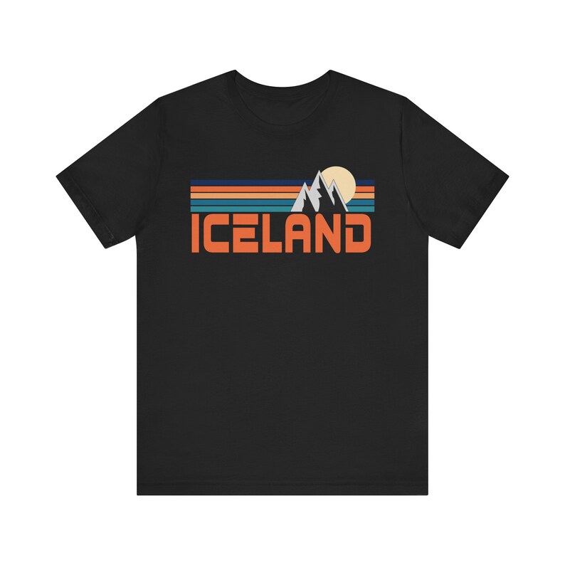 Puede incluir: Camiseta negra con un gr&aacute;fico retro de monta&ntilde;as y un sol con la palabra "ICELAND" en letras naranjas.