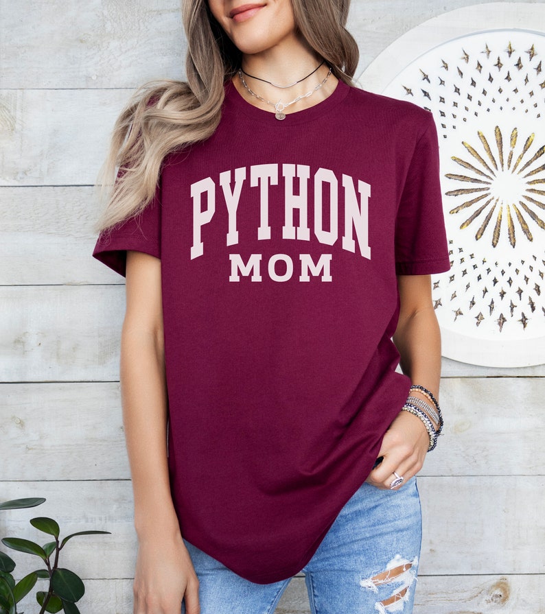 Peut inclure: Un t-shirt bordeaux avec le texte "PYTHON MOM" en blanc.