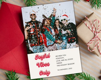 May include: A Christmas card with a photo of four friends wearing festive sweaters and celebrating with confetti. The card has the text "Joyful Vibes Only" in red and white letters and a message wishing positivity, love, and all good things this holiday season. The card is signed "The Shepherds | 2022".