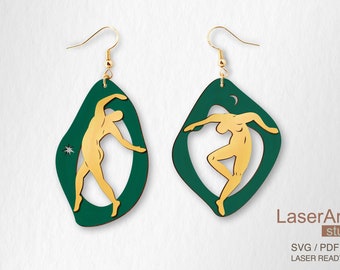 May include: A pair of gold-colored figure earrings with a dark green border. One earring has a star, the other a crescent moon. The earrings are laser-cut and feature a dancer design. The earrings are suspended from gold-colored hooks.