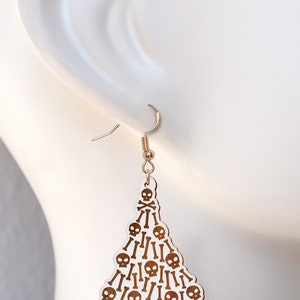 May include: White dangle earrings shaped like a Christmas tree with gold skulls and crossbones.