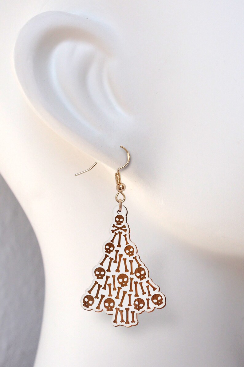 May include: White dangle earrings shaped like a Christmas tree with gold skulls and crossbones.