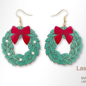 May include: A pair of green and red Christmas wreath earrings with a red bow and white pearl accents. The earrings are made of wood and have a gold hook.